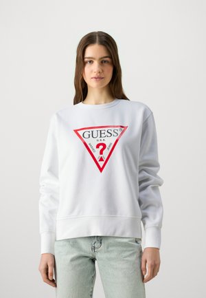 Biela mikina s červeným trojuholníkovým logom a textom "GUESS" a otáznikom, vyrobená z mäkkého materiálu s rebrovanými manžetami a lemom.