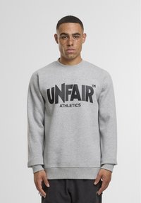 Grijze trui met een ronde halslijn en manchetten, met een grote zwarte "UNFAIR ATHLETICS" logo aan de voorkant. Zachte fleece stof.