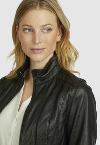 Black leather jacket with a zippered front, high collar, and vertical seam detailing. Worn over a white blouse. Smooth texture.