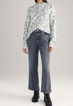 Un léger pull à motif moucheté en crème et marine, associé à un jean gris taille haute, avec une jambe droite et un ourlet effiloché.