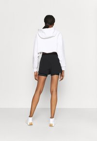 Sudadera blanca recortada con capucha, combinada con pantalones cortos negros. Los pantalones cortos tienen un corte relajado y están recortados en el dobladillo. Calzado blanco.