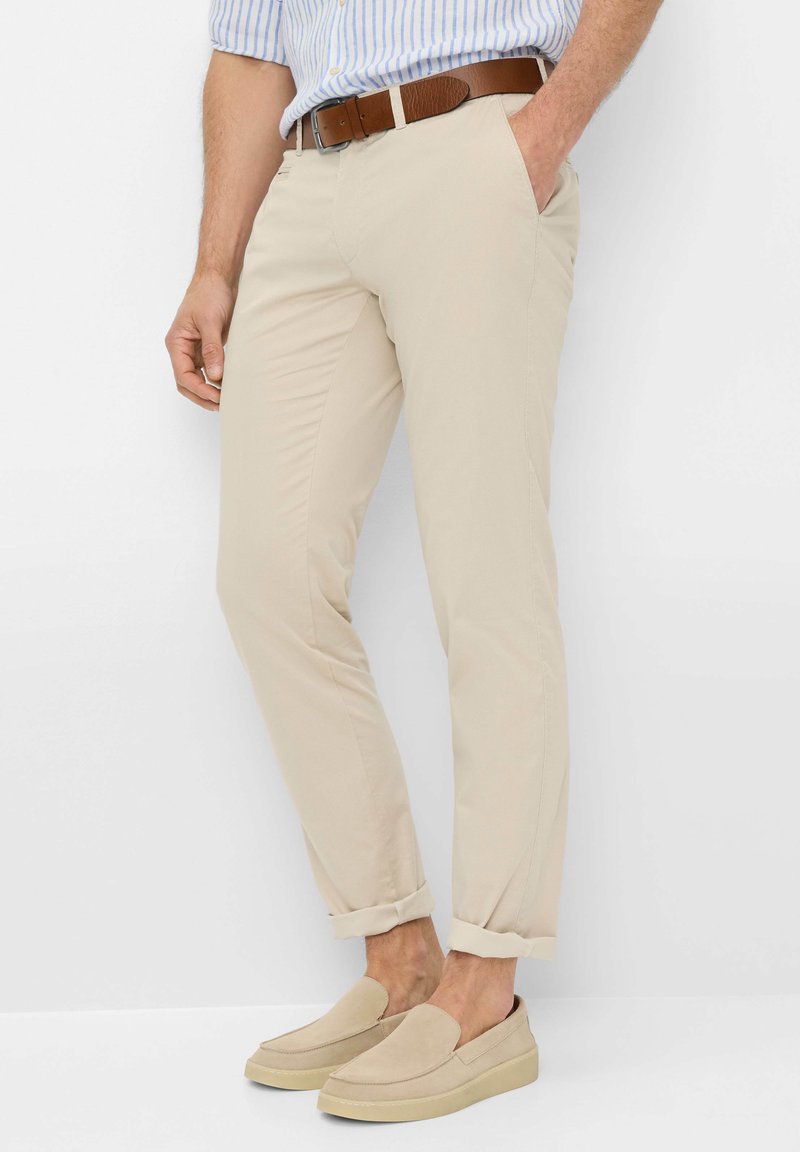 Chinos beige con una vestibilità slim, realizzati in cotone. Presentano orli arrotolati, tasche laterali e una cintura in pelle marrone. Abbinati a scarpe slip-on beige.