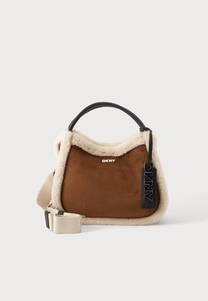 Hnedá semišová kabelka s krémovým shearling lemovaním, čiernou rukoväťou, béžovým nastaviteľným remienkom a DKNY logo na prednej strane.
