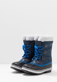 Niebieskie i czarne śniegowce z puszystym białym wykończeniem, wodoodporny materiał, teksturowane gumowe podeszwy i okrągłe sznurowadła zapewniające pewne dopasowanie.