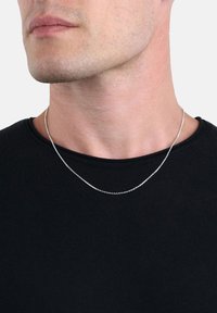 Collana di catena d'argento su un collo nudo, con un design semplice e piccoli anelli rotondi, posizionata su una camicia nera.