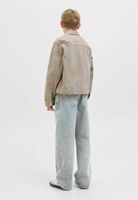 Veste en denim kaki à coupe droite, avec des manches longues et des poignets à boutons, associée à un jean large bleu clair et des baskets.