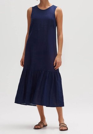 Ärmelloses, marineblaues Midikleid mit gerafftem Saum, getragen mit schwarzen, flachen Riemchensandalen vor neutralem Hintergrund.