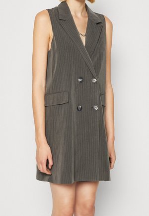 Sleeveless charcoal gray pinstripe double-breasted vest dress with notch lapels and flap pockets, worn by a standing person.