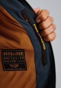 Navy-Jackett-Innenleben mit orangefarbenem Netzfutter. Enthält ein Etikett mit "SKYGLIDER", Designdetails und einem schwarzen Etikett mit der Aufschrift "PME LEGEND."