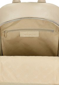 Beżowe, teksturowane wnętrze plecaka ze skóry, z kieszonką na zamek, wykończone gładką podszewką i brązową metką. Miękki, pikowany detal z tkaniny.