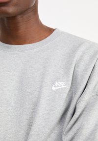 Sweatshirt de algodão cinzento com decote redondo. Apresenta um pequeno logótipo da Nike em branco bordado no peito. Textura suave com um ajuste descontraído.
