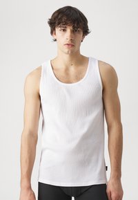 Hvit tanktop laget av ribbestrikket stoff, med rund hals og brede skulderstropper. Glatt tekstur med minimal detaljer.
