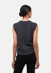 Pull en tricot sans manches de couleur gris foncé avec un col et un ourlet côtelés, mettant en valeur un tissu texturé et une silhouette ajustée.