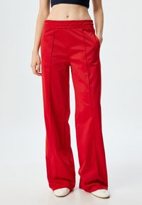 Rote, hoch taillierte, weite Hosen aus glattem Stoff mit seitlichen Taschen; mit dekorativen Nähten an der Vorderseite.