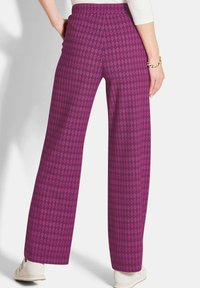 Weite Hose aus einem lebhaften lila Stoff mit einem Rautenmuster. Elastischer Bund und glatte Textur. Keine sichtbaren Beschläge oder Akzente.