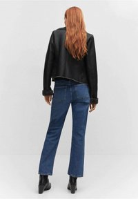 Veste cropped en cuir noir avec doublure en fourrure, associée à un jean en denim bleu droit et des bottines à talons noires. Détails de couture visibles.