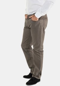 Chinos de algodón grises con bolsillos laterales y detalles de costura sutil, combinados con zapatos negros. El corte es slim y ajustado.