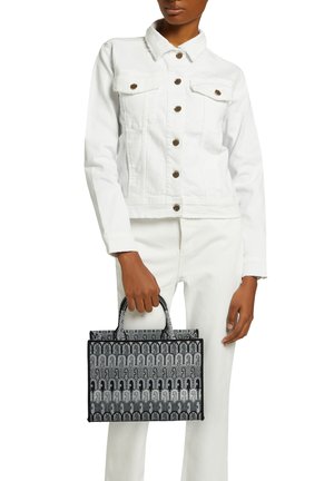 Sac fourre-tout à motif noir et blanc avec deux poignées supérieures, de forme rectangulaire et avec une surface texturée. Porté avec une veste en denim blanche et un jean.