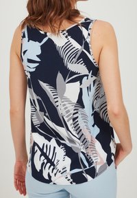 Top sin mangas en azul marino con un estampado de hojas tropicales. Presenta acentos en gris claro, blanco y tonos pastel. Textura suave con un dobladillo redondeado.