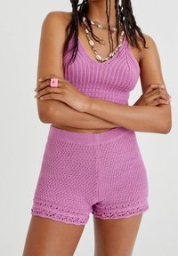 Szydełkowy zestaw składający się z dwóch części w pastelowym różowym kolorze, zawierający crop top z dekoltem w kształcie litery V oraz pasujące szorty z koronkowym wykończeniem na końcu. Materiał o ciekawej teksturze.