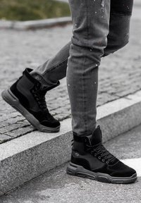 Sneakers neri alto realizzati con una combinazione di pelle scamosciata e materiale tessile, dotati di una suola spessa e supporto alla caviglia rinforzato.