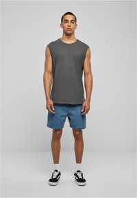 T-shirt sans manches gris, shorts en denim, baskets noir et blanc. Look simple et décontracté avec une coupe ample, sans motifs ni accents visibles.