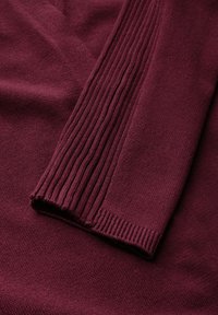 Burgunderfarbener Pullover mit einer glatten Stricktextur, der gerippte Bündchen und eine lässige Passform aufweist. Ein weicher, kuscheliger Stoff mit engmaschigen Designdetails.