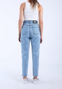 Ljusblå högmidjade jeans med raka ben och två bakfickor. Avslutade med en svart etikett vid midjan och bärs med vita sneakers.