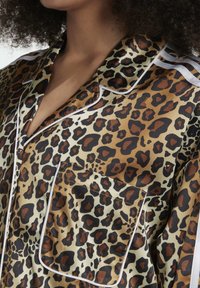 Lepardmönstrad satinsskjorta med en ljus gräddbas, bruna och svarta fläckar, vit kant och en bröstficka.