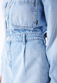 Lys blå denimkjole med fitted talje, knaplukning, brystlommer og synlige sømdetaljer. Glat tekstur med let falmning.