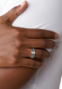 Anillo de banda de plata con grabado, que presenta un acabado suave y pulido. La mano del usuario descansa sobre una superficie de tela blanca.