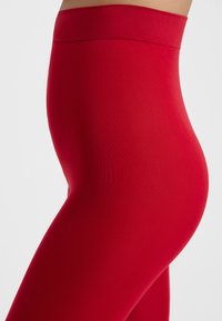 Leggings rojos de cintura alta hechos de una tela elástica, con una textura suave y un corte ceñido, sin costuras visibles.