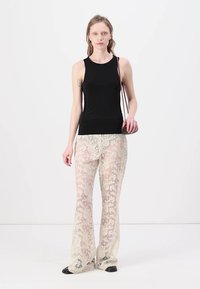 Haut sans manches noir associé à un pantalon en dentelle transparente avec un motif floral en blanc cassé, présentant une silhouette ajustée et des jambes évasées.