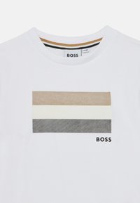 Λευκό βαμβακερό t-shirt με οριζόντιες ρίγες σε τόνους ταμπά, κρεμ και γκρι. Μαύρο λογότυπο "BOSS" τυπωμένο κάτω δεξιά.
