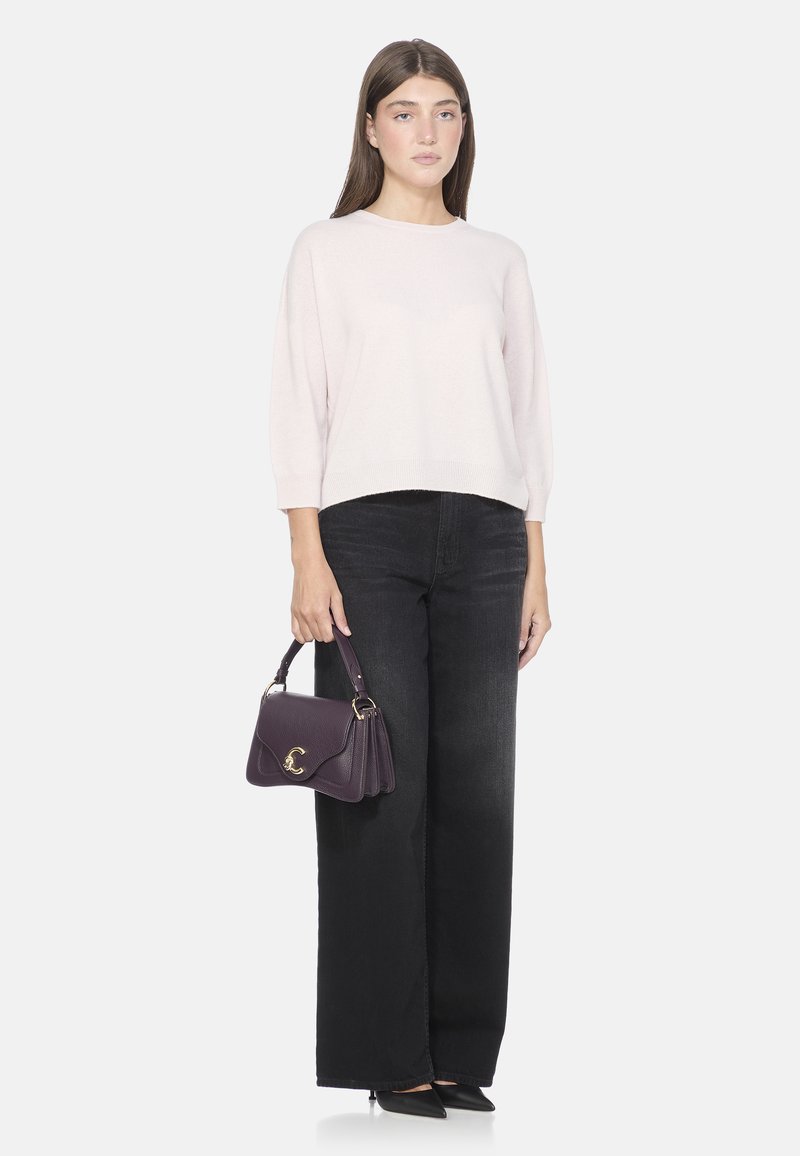 Maglione a maglia rosa chiaro con maniche a tre quarti, abbinato a jeans neri a vita alta e a gamba larga. Tiene una borsa viola con dettagli dorati.