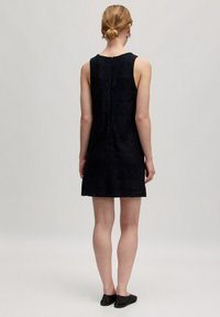 Ärmelloses schwarzes Kleid mit strukturierten geometrischen Mustern, knielang, mit einem Reißverschluss auf der Rückseite und einer lockeren Passform. Kombiniert mit schwarzen flachen Schuhen.