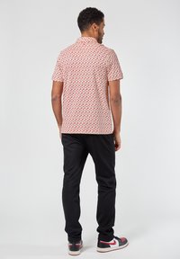 Korte mouwen shirt met een rood bloemenpatroon op een lichte achtergrond, gecombineerd met zwarte broek en multikleuren sneakers.