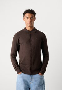 Bruin button-up cardigan met een gekraagde halslijn, lange mouwen en geribbelde manchetten, gecombineerd met lichtblauwe spijkerbroek.
