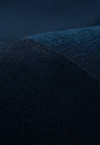 Tejido de color azul oscuro que muestra una textura entrelazada, con un acabado suave y sutiles variaciones en color y luz, destacando su profundidad y riqueza.