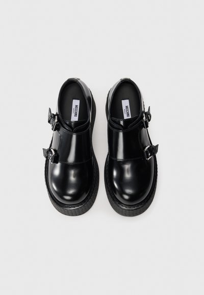 Pair of black shiny leather platform shoes with double buckle straps and Moschino labels inside, shown from above on white background.