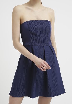 Robe sans bretelles bleu marine avec un corsage structuré, un tissu texturé, une jupe plissée et une taille ajustée.
