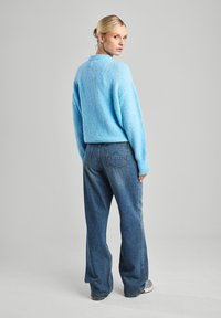 Un pull en maille bleu clair avec un col rond et des poignets côtelés, associé à un jean taille haute bleu foncé avec des poches arrière.