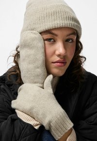 Beigen värinen neulottu pipo ja rukkaset, jotka on valmistettu pehmeästä langasta. Pipossa on resorikuvio, kun taas rukkaset ovat leveät ja niiden pinta on teksturoitu.