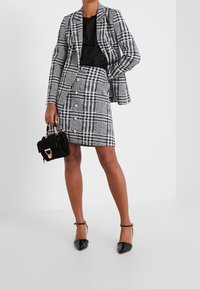 Conjunto de blazer y falda de patrón de cuadros en blanco y negro, en tejido texturizado, con grandes botones, acompañado de un bolso negro y tacones de charol.