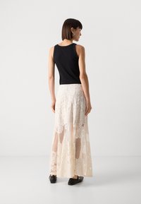 Black sleeveless top paired with a long, beige lace skirt featuring floral patterns and mesh accents, complemented by black shoes.