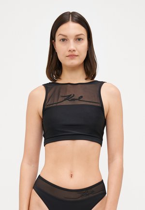 Black crop top featuring a sheer mesh front, embroidered logo, and a fitted design. Material has a smooth texture with a cropped cut.