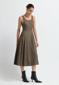 Vestido marrón sin mangas con rayas verticales,Silhouette en A, de largo a la rodilla, tejido texturizado. Combinado con botines negros hasta el tobillo.