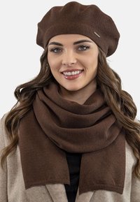 Bruine wollen baret en sjaal, met een zachte textuur en een gladde afwerking. De sjaal valt elegant, zonder zichtbare patronen of accessoires.