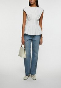 Hvid bomulds peplum top med kapærmer, plisseret design ved taljen, parret med lyseblå lige ben jeans og en lille hvid håndtaske.