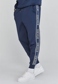 Marine joggers van een lichtgewicht stof met elastische boorden, voorzien van een witte logo-streep aan de zijkant en zakken voor functionaliteit.